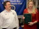 News 12 Long Island reporter Jackie Lukas received the 2015 Leonard Award from Great South Bay ARC President John Melfi, W2HCB (left), at the March 2016 meeting of the Great South Bay Amateur Radio Club. [Kevin Morgan, AB2ZI, photo]